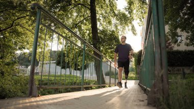 Güneşli bir akşamda ağaçlarla çevrili bir yolda yürüyen bir adam. Sahne sakin ve doğal..