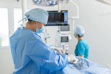 Steril giyimli iki tıp uzmanı modern bir ameliyathanede cerrahi müdahaleye hazırlanıyorlar..