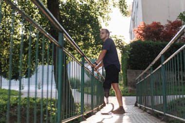 Koşmak ve yürümek için protez bacağı olan aktif bir adam, küçük bir park köprüsünde duruyor, açık havanın tadını çıkarıyor. Güç ve özgürlük kavramı.