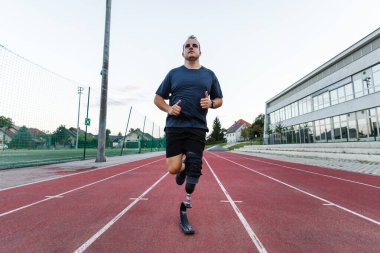 Erkek sporcu güvenli ve kendinden emin bir şekilde bir spor bıçağıyla transtibiyal protez kullanarak koşuyor ve aktif bir hayatın tadını çıkarıyor..