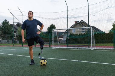 Bir adam akşam boyunca yeşil bir sahada futbol oynarken protez bacak kullanıyor..