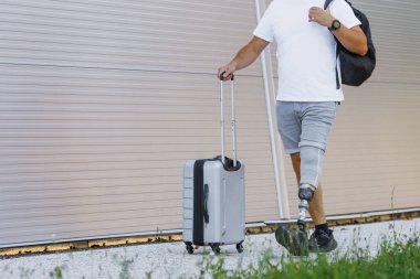 Protez bacaklı bir adam tramvay çantasını cadde boyunca yuvarlıyor. Engellilik, hareket kabiliyeti ve seyahat konsepti.