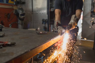 Gözlüklü ve güvenlik eldivenli bir adam atölyede plazma kesici ile çalışırken kıvılcım çıkartıyor..