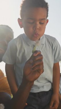 Güneşli bir çayırda dinlenirken, Afrikalı bir Amerikalı baba ve iki oğlu eğleniyor, karahindiba üflüyor ve birlikte gülüyorlar.