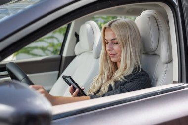 Kadın araba kullanırken elinde telefon ve mesaj tutuyor..
