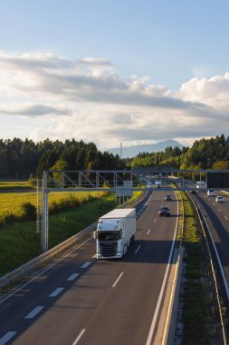 Tarlalar ve ağaçlarla çevrili bir otoyolda giden kamyonlar, nakliyeyi kolaylaştırıyor ve dağıtım ağlarını destekliyor.