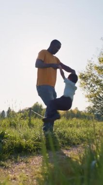 Afro-Amerikan bir baba ve gülümseyen oğlunun açık havada oynaması, birlikte eğlenmesi, babasının küçük oğlunu döndürmesi.