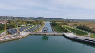 Su kenarında güneş panelleri olan bir hidroelektrik santralinin hava görüntüsü yenilenebilir enerji üretimi ve altyapısını gösteriyor..