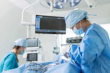 Kadın cerrahi ekibi, gelişmiş ekipman ve steril koşullarla temiz bir hastane ameliyathanesinde tıbbi işlem gerçekleştiriyor..