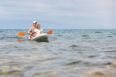 Erkek ve kız kardeşler mavi gökyüzü ve güneşin altında ayakta sörf yapmayı severler. Birlikte eğlenceli bir anı paylaşıyorlar..