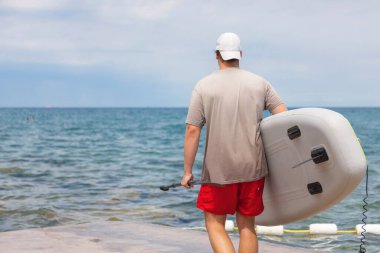 Genç bir adam açık bir yaz günü plajda suya doğru kürek çekerek yürür. Deniz kenarındaki açık hava aktivitelerini sever..