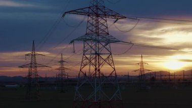 Yüksek voltajlı elektrik santrali tersanesi kırsal bir alanda gün batımında trafolar ve iletim hatlarını gösteriyor..