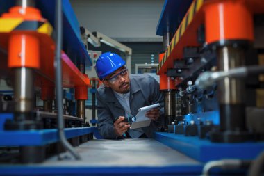 Afrika kökenli Amerikalı bir mühendis, kalite kontrol ve bakım için bir fabrikada makine ve ekipmanları kontrol ediyor. Güvenlik protokollerini takip ediyor..