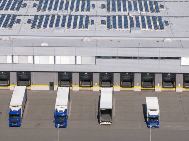 Kamyonlar bir lojistik merkezindeki yükleme rıhtımına park edilmiş. Güneş panelleri çatıda. Bu bölge kargo ve nakliye işleriyle ilgilenir..