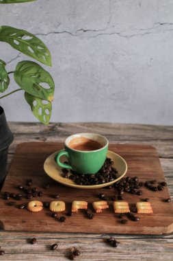 Beyaz fincanda kahve, kavrulmuş kahve çekirdekleri ve ahşap arka planda küçük bir İngiliz harfi çıtır ekmek. Uzayı kopyala Yukarıdan bak. Yatay yönelim.