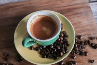 Beyaz fincanda kahve, kavrulmuş kahve çekirdekleri ve ahşap arka planda küçük bir İngiliz harfi çıtır ekmek. Uzayı kopyala Yukarıdan bak. Yatay yönelim.