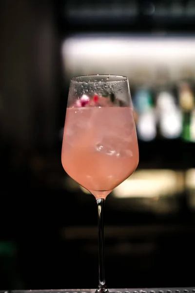 A gourmet mixed drink cocktail of sweet pink lemonade vodka and gin martini, garnished in the bar with bottles in the dark background
