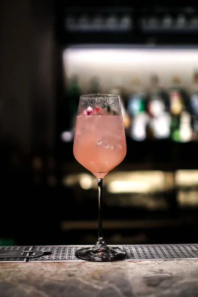 A gourmet mixed drink cocktail of sweet pink lemonade vodka and gin martini, garnished in the bar with bottles in the dark background