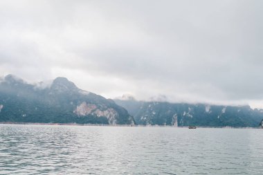 Yüzthani Tayland 'daki Khao Sok Ulusal Parkı' nda bulutlu gün batımı gökyüzü, deniz ve dağlar ile kıyı şeridi. Alacakaranlık döneminde doğa. Denizin üzerinde gün doğumu da dahil..