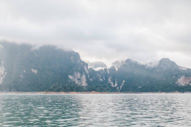 Yüzthani Tayland 'daki Khao Sok Ulusal Parkı' nda bulutlu gün batımı gökyüzü, deniz ve dağlar ile kıyı şeridi. Alacakaranlık döneminde doğa. Denizin üzerinde gün doğumu da dahil..