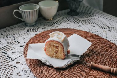 Limonlu pasta dilimi, seramik tabakta şekerli krema, çatal, limon ve ahşap kaplama..