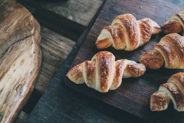 Pastanenin rafındaki kruvasanlar ahşap kesim tahtasını gösteriyor. Yemek yaşam tarzı, seçici odaklanma. Sıcak Taze Tereyağlı Kruvasan..