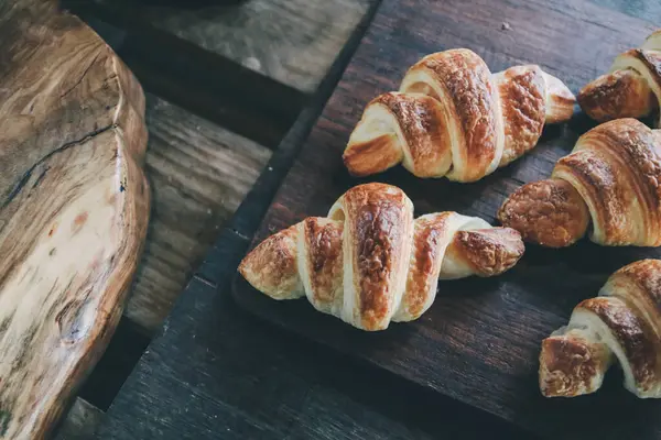 Pastanenin rafındaki kruvasanlar ahşap kesim tahtasını gösteriyor. Yemek yaşam tarzı, seçici odaklanma. Sıcak Taze Tereyağlı Kruvasan..
