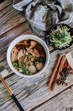 Domuz eti ve sebzeli erişte ve beş baharatlı, ahşap masa üstünde siyah çorba. Asya yemeği tarzı..