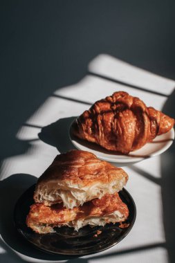 Sabah ışığında karanlık bir arka planda kruvasanlar, güneş ışığı gölgesi. Sabah kahvaltısı kavramı. Boşluğu kopyala.