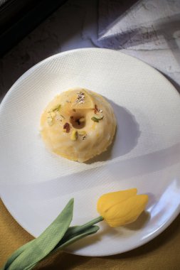 Sarı laleli limonlu pasta, klasik tarif, koyu arkaplanda beyaz seramik tabakla süslenmiş.