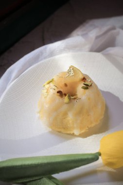 Sarı laleli limonlu pasta, klasik tarif, koyu arkaplanda beyaz seramik tabakla süslenmiş.