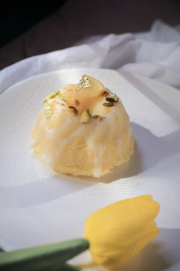 Sarı laleli limonlu pasta, klasik tarif, koyu arkaplanda beyaz seramik tabakla süslenmiş.