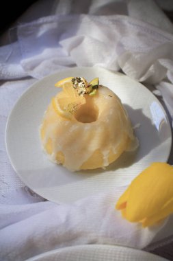 Sarı laleli limonlu pasta, klasik tarif, koyu arkaplanda beyaz seramik tabakla süslenmiş.