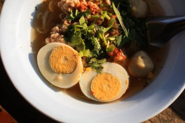 Rice vermicelli Noodle soup with pork balls and egg in white bowl on wooden terrace under sunlight.