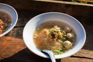 Rice vermicelli Noodle soup with pork balls and egg in white bowl on wooden terrace under sunlight.