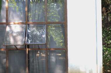 Kır evindeki bahçe banyosunun güneş ışığıyla kaplı kırsal metal penceresi. Terk edilme binası ve çürüme.