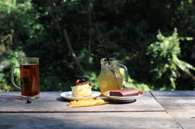 Bask peynirli kek, çilekli kek, çikolatalı kek ve ferahlatıcı içecek. Ahşap masada nefis ev yapımı hamur işi..