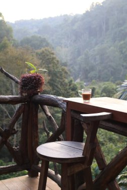 Orman manzaralı ahşap teras masasında sıcak kahve. Kahvaltı Tazeleniyor.