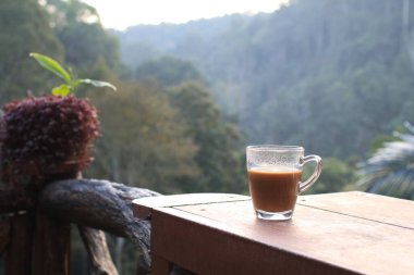 Orman manzaralı ahşap teras masasında sıcak kahve. Kahvaltı Tazeleniyor.