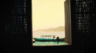 Koh Sdach Adası 'nda sakin bir denizde geleneksel bir Khmer teknesinin manzarasına giden açık bir pencereye doğru yürüyorum.