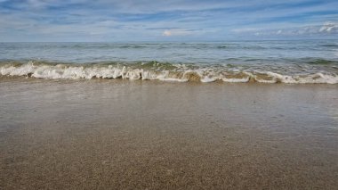 Sakin okyanus dalgaları parçalı bulutlu bir gökyüzünün altındaki kumlu bir plaja doğru hafifçe süzülüyor ufuk çizgisi gökyüzündeki gök mavisi suyu ikiye ayırıyor. Sipalay, Negros Batı, Filipinler