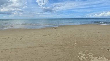 Bulutlu mavi gökyüzünün altında kumlu sahil