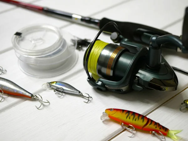 Fishing tackles lay on white wooden boards. Set of fishing tackles. Close up view on spool, rod, wobblers and lines.