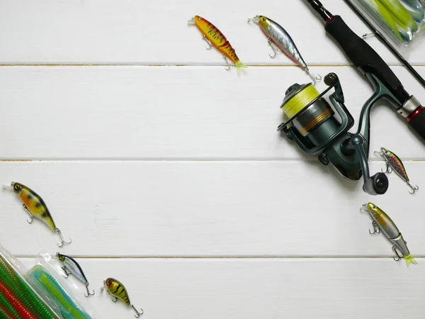 Fishing tackles lay on white wooden boards. Set of fishing tackles. Top view on spool, rod, spoons, wobblers and lures.