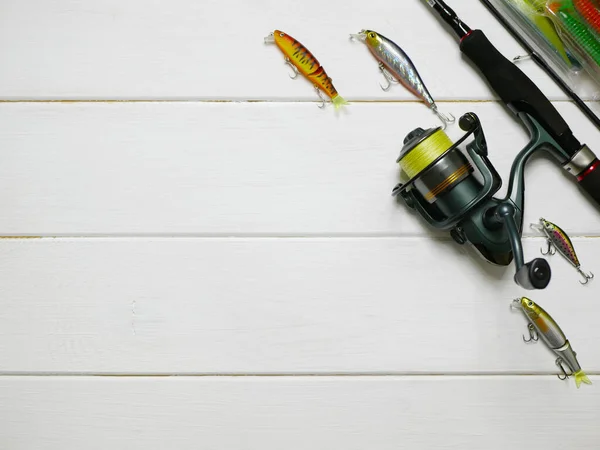 Fishing tackles lay on white wooden boards. Set of fishing tackles. Top view on spool, rod, wobblers and lures.