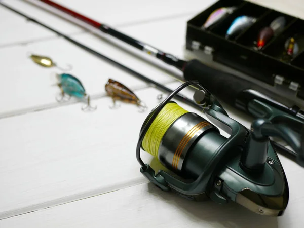 Fishing tackles lay on white wooden boards. Set of fishing tackles. Close up view on spool, rod, wobblers and lure box.