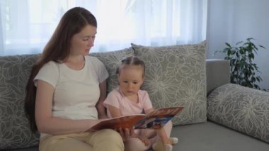 Anne ve kızı çocuk kitabı okuyorlar. Anne ve kızı birlikte vakit geçiriyorlar ve kitap izliyorlar. Aile üyeleri konuşuyor..
