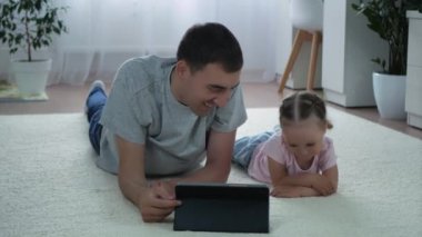 Bir kız ve bir baba tabletten komik bir şey izleyip evde yerde yatıyorlar. Küçük bir kız ve mutlu bir baba birlikte vakit geçiriyorlar. Şirin küçük kız evde babasıyla müzik dinliyor..