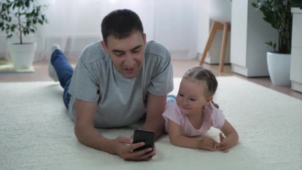 Dochter Vader Kijken Iets Grappigs Smartphone Liggen Thuis Vloer Schattig — Stockvideo