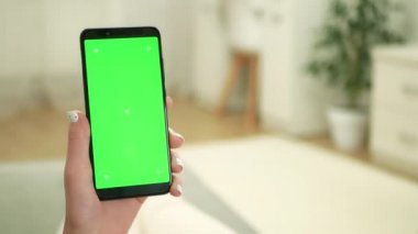 Kadın kanepeye uzanır ve yeşil ekranlı akıllı telefonu tutar. Kadının elinde yeşil ekranlı siyah akıllı telefon var. Renkli anahtar arkaplana sahip dijital aygıt.
